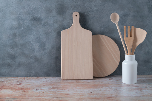 Modern kitchen kitchenware in light wood color with ladle, cutting boards and cookware on gray