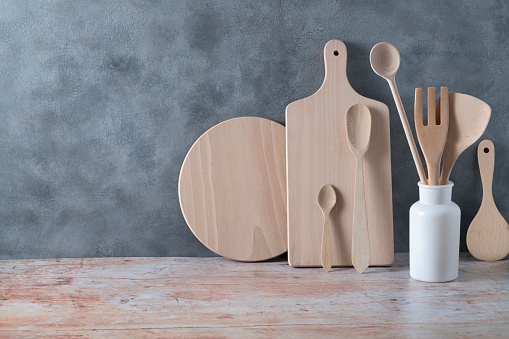 Modern kitchen kitchenware in light wood color with ladle, cutting boards and cookware on contemporary gray cement wall