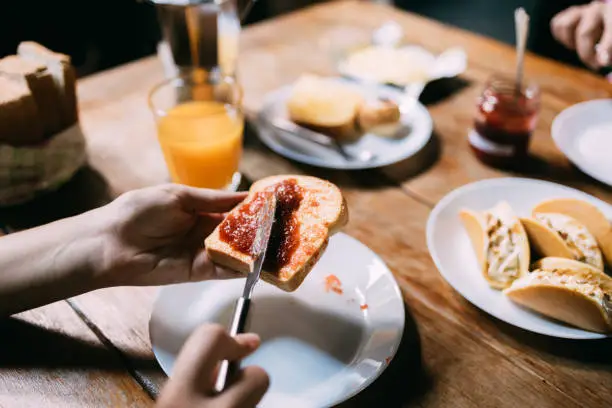 Close up shot of an anonymous woman spreading jam on a piece of bread.