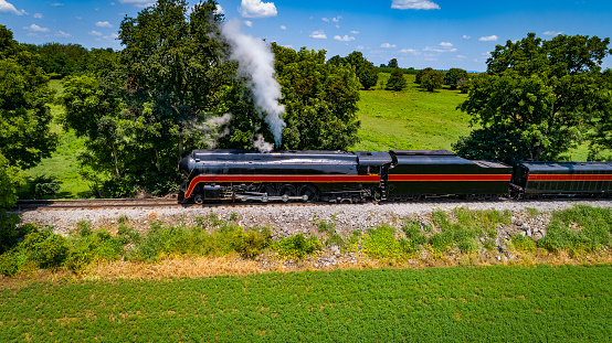 Side Aerial View of a Steam Streamlined Locomotive Blowing Smoke on a Beautiful Summer Day
