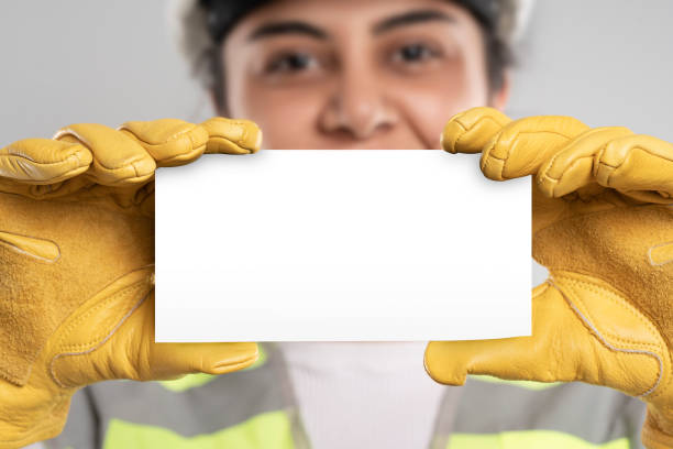 A female engineer with white safety helmet, yellow safety gloves and reflective vest. Hands holding checklist for writing and checking