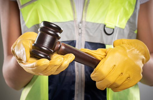 A female engineer with yellow safety gloves and reflective vest. She is holding a gavel.