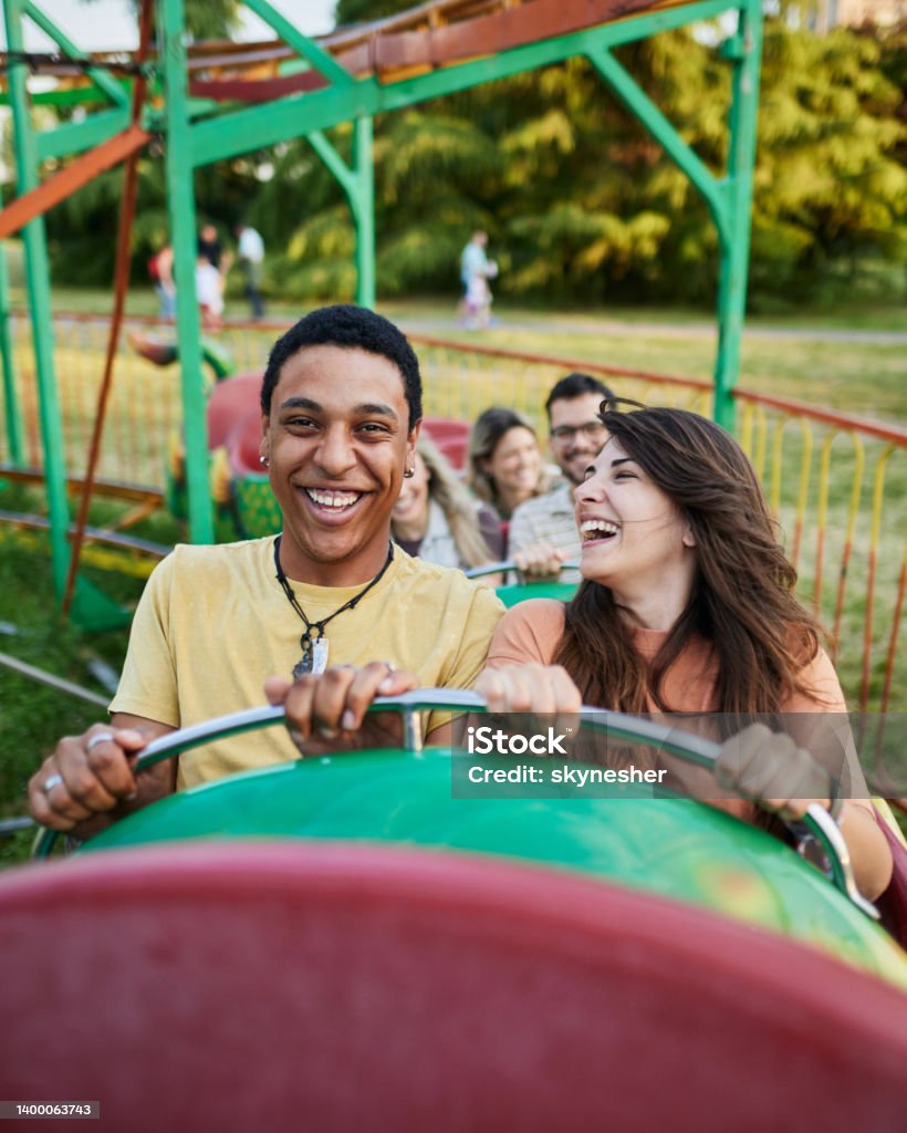 Happy couple having fun while riding on rollercoaster at amusement park. Young happy couple having fun on rollercoaster at amusement park. Rollercoaster Stock Photo