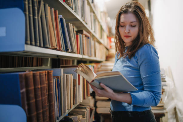 istock Beautiful university student standing by the shelf in the library and going through a book 1400064124