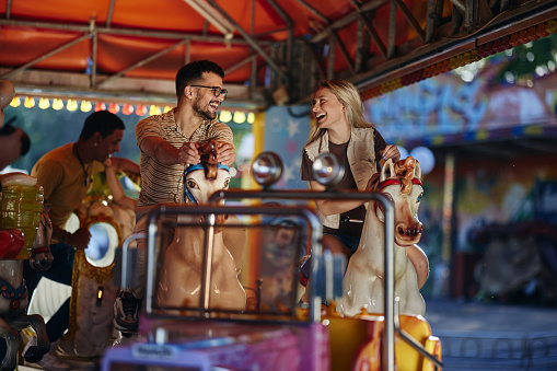 Young happy couple communicating while having fun on carousel at amusement park.