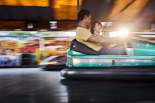 Young happy couple having fun in bumper car at amusement park. Blurred motion. Copy space.
