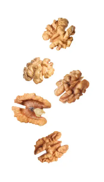 Photo of Halves of walnuts falling on white background
