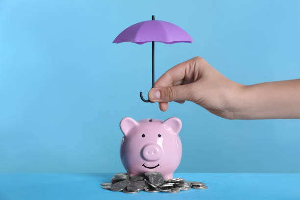 femme tenant un petit parapluie au-dessus d’une tirelire avec des pièces de monnaie sur fond bleu clair, gros plan - umbrella protection savings currency photos et images de collection
