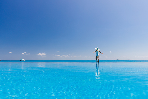 Rear view of carefree woman with her arms outstretched at the edge of an infinity pool in summer day. Copy space.