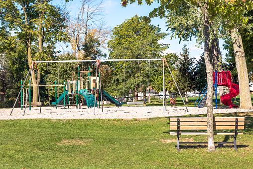 Deserted playground for children with slides and swings in a public park on a sunny autumn day. Gananoque, ON, Canada.