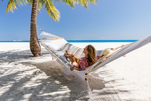 Happy woman enjoying while relaxing in hammock during summer day on the beach.