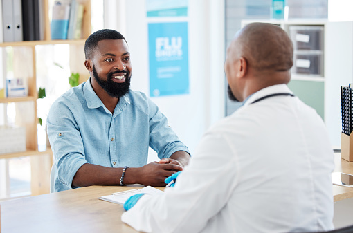 Young man in consult with his doctor. African man talking his gp in a checkup. Confident man talking to a medical specialist in the hospital. Medical professional talking to patient in the clinic