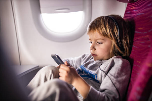 niño pequeño viendo dibujos animados en un teléfono inteligente en el avión. - telephone cabin fotografías e imágenes de stock