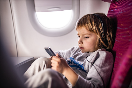 Relaxed little boy using mobile phone while traveling by airplane.
