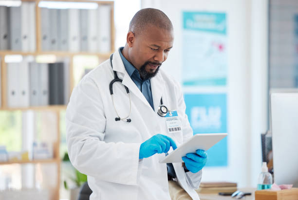 istock Focused doctor using a digital tablet in his clinic office. African american specialist using an online device. Caring gp wearing gloves using a wireless digital device. 1400066857