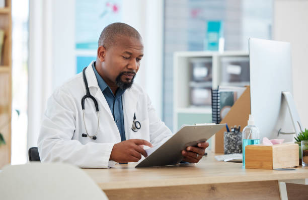 istock Mature african american doctor checking a patients chart. Focused gp reading a chart on a clipboard. Serious doctor reading a patients report. Professional physician reading a medical document 1400066883