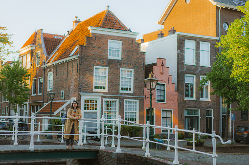 Young Caucasian woman standing on the bridge above the canal  in Leiden town at sunset
