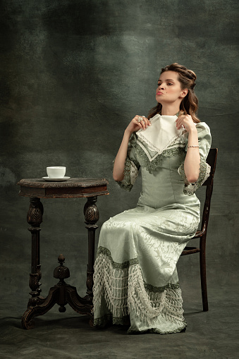 Put on airs and graces. Portrait of young beautiful girl in gray dress of medieval fashion style isolated on dark background. Comparison of eras concept, flemish style. Classic art character, old-fashioned.