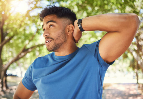 istock Fit athletic man smiling while stretching his arms during a workout at the park. Hispanic man doing warm-up exercises outdoors on a sunny day. Athletic man taking a break from a fitness routine 1400070341