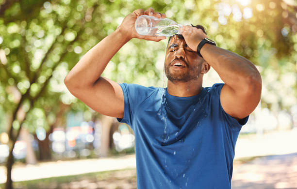 istock Young mixed race athletic man splashing his head with water and staying hydrated while focused on health and fitness. Thirsty man taking a break from exercising and cooling his face on a summer day 1400070344