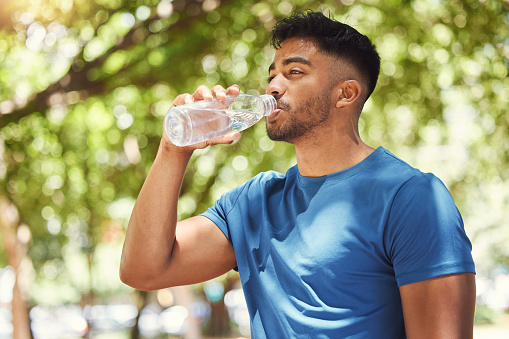 Young mixed race athletic man drinking water and staying hydrated while focused on his health and fitness. Thirsty man taking a break from exercising and drinking from bottle while training outside