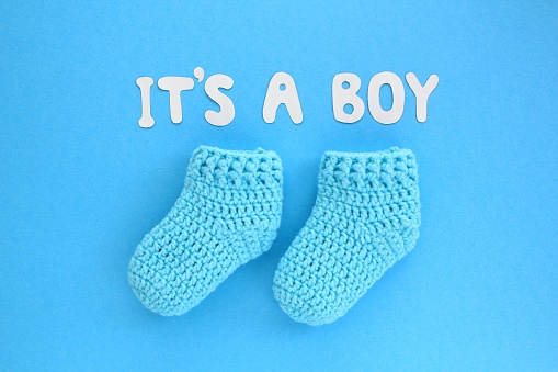It's a boy lettering, crochet baby booties on blue background. Baby boy birth, new life, family concept. Greeting card idea for newborn. Pregnancy announcement. Flatlay, top view