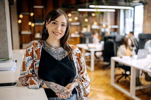Young beautiful smiling tattooed woman posing in the office