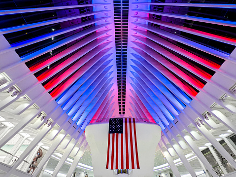 New York, NY, USA - May 29, 2022: Inside the Oculus/ World Trade Center Transportation Hub, designed by Santiago Calatrava, located in downtown Manhattan. Red and Blue lights illuminate the ceiling along with a prominent display of the American flag.