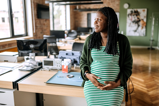 Young casually clothed pregnant businesswoman posing in the office