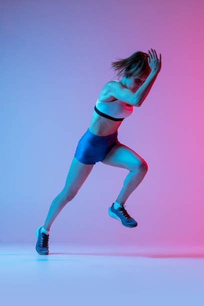 istock Studio shot of professional female athlete, runner training isolated on pink studio background with blue neon filter, light. Concept of action, motion, speed 1400075873
