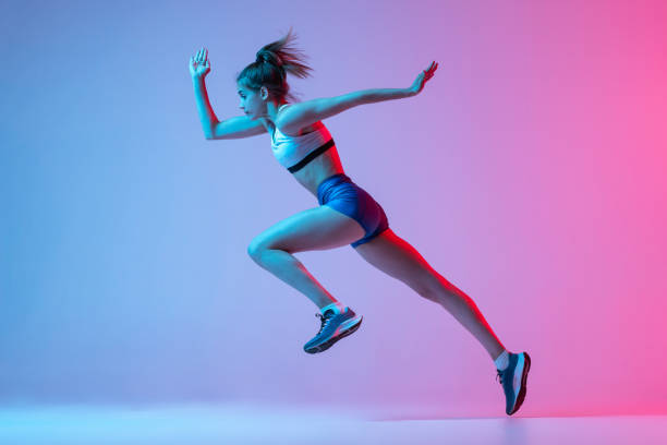 istock Studio shot of professional female athlete, runner training isolated on pink studio background with blue neon filter, light. Concept of action, motion, speed 1400075875