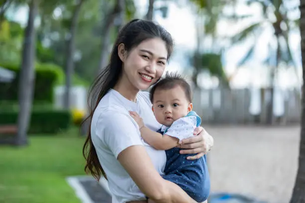 Happy Asian mom holding her newborn baby smile and spending time for good moment together. Adorable little baby boy having fun and cheerful with love from mother.Mother day concept