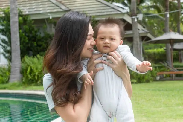 Happy Asian mom kissing her newborn baby smile and spending time for good moment together. Adorable little baby boy having fun and cheerful with love from mother.Mother day concept