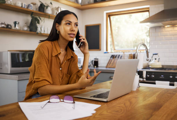 istock Young serious mixed race businesswoman going through paper and bills while on a call using her phone and working on a laptop at home. One hispanic female businessperson using a laptop and talking on a phone while planning her business 1400082365