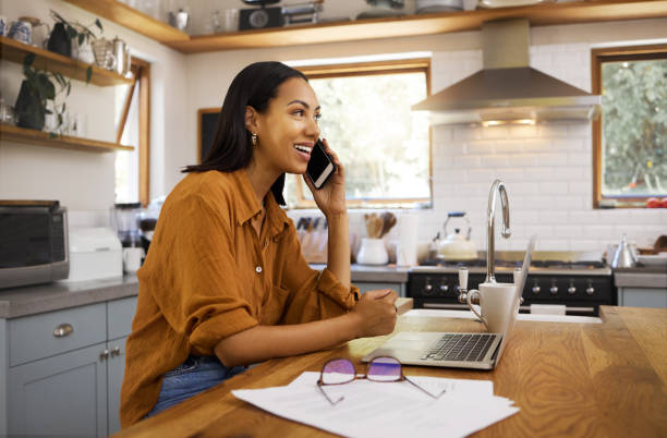 istock Young cheerful mixed race businesswoman going through paper and bills while on a call using her phone and working on a laptop at home. One hispanic female businessperson using a laptop and talking on a phone while banking at home 1400082381