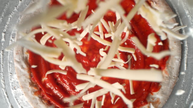 Grated Cheese Falling onto Round Rolled Pizza Dough Spread with Tomato Sauce - Table Top View