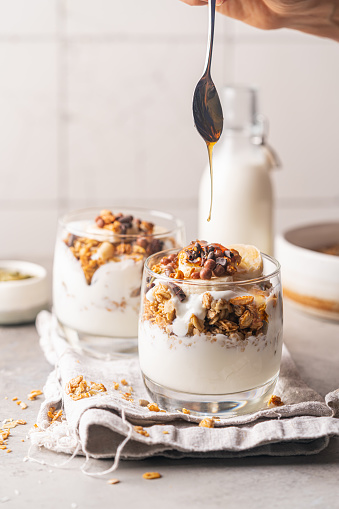 Glass of granola parfait with banana, nuts, chocolate and honey. Healthy breakfast concept.