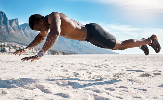 Fit young black man doing plank hold exercises on sand at the beach in the morning. African American muscular male bodybuilder athlete doing bodyweight workout to build a strong core and endurance