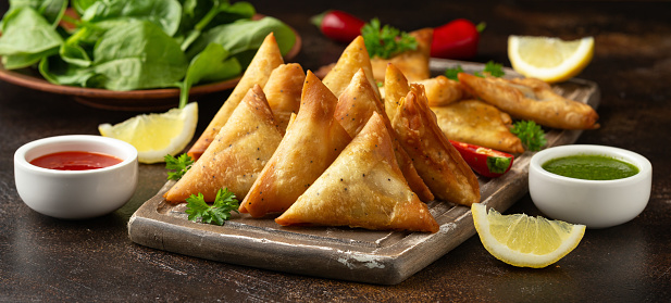 Fried samosas with vegetable filling, popular Indian snacks on wooden board.