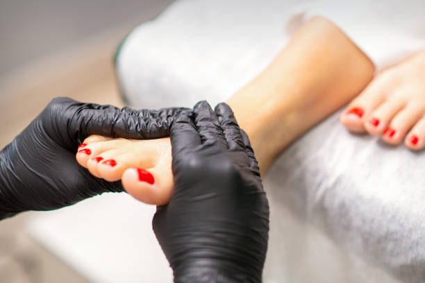 massage des pieds avec crème hydratante et peeling par des mains pédicures portant des gants noirs, en gros plan. - reflexology pedicure massaging human foot photos et images de collection