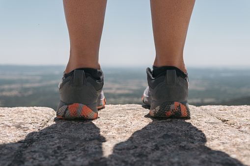 Man or woman wearing trekking shoes peering over the edge of a high-altitude trail to see the beautiful views.