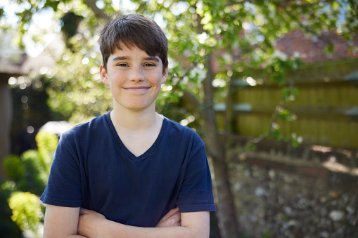 Portrait Of Smiling Teenage Boy With Crossed Arms Standing In Summer Garden At Home