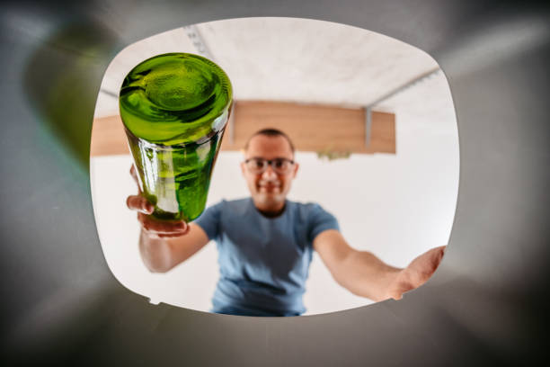 Young Man Putting Glass Bottle In The Recycling Bin