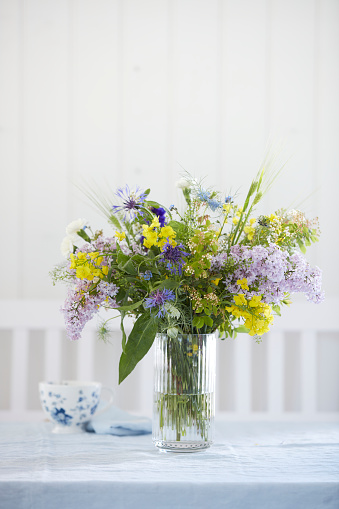 Bouquet of flowers in glass vase on table, with cup and white bench in background