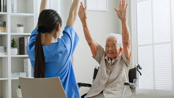 Young Asian woman nurse, caregiver assist a senior Asian woman to do physical therapy and exercise arms at home stock photo