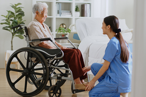 Young Asian woman, nurse, caregiver, carer help and assist a senior Asian woman on wheelchair at home
