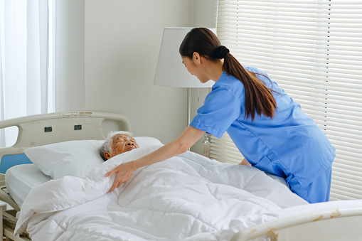 Young Asian woman, nurse, caregiver, carer of nursing home take care and cover a senior Asian woman with blanket at home.