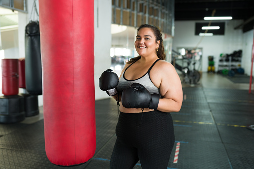 Cheerful plus size woman smiling and looking at the camera while practicing box at the gym