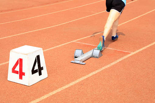 A large group of legs in a walking race with a pavement foreground. Depth of field is very shallow with clear focus on the second row of feet only.