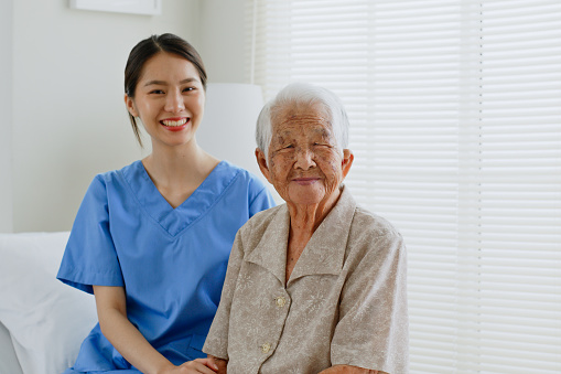 Portrait of young Asian woman, nurse, caregiver, carer of nursing home and senior Asian woman smiling at home. Look at camera